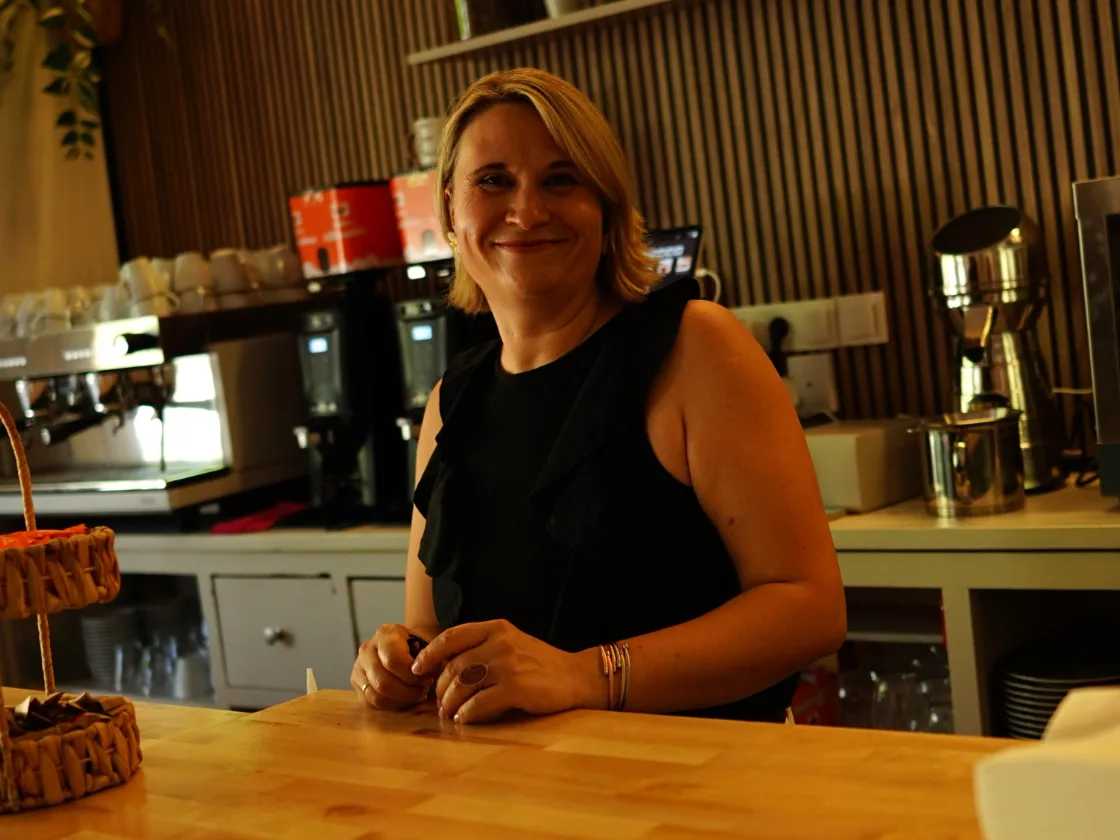 Eli, sonriendo detrás de la barra de su cafetería
