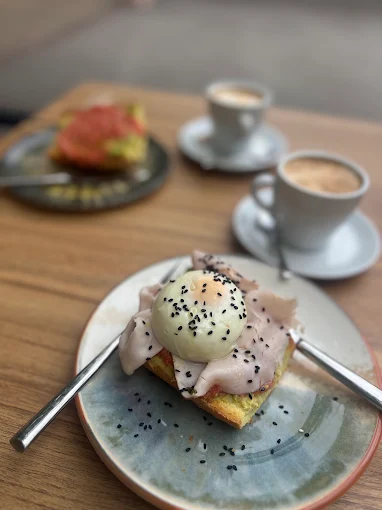 Tostada con huevo poché, jamón y sésamo negro, con dos cafés al fondo